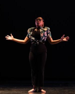 Ma’Kyia Frazier stands alone on stage, facing the audience with her arms open. 